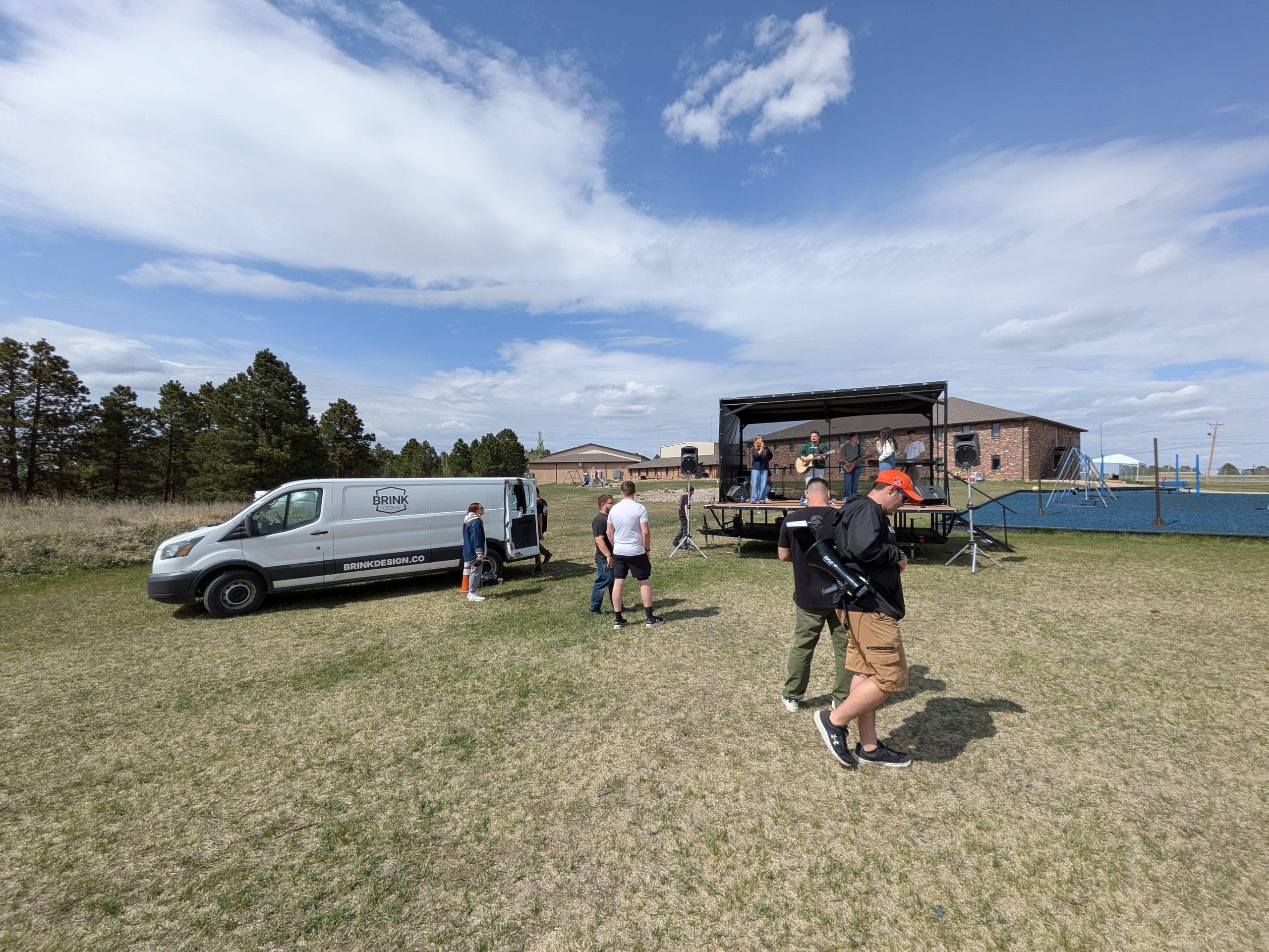 The worship band on the covered trailer stage, with the van parked nearby on the field