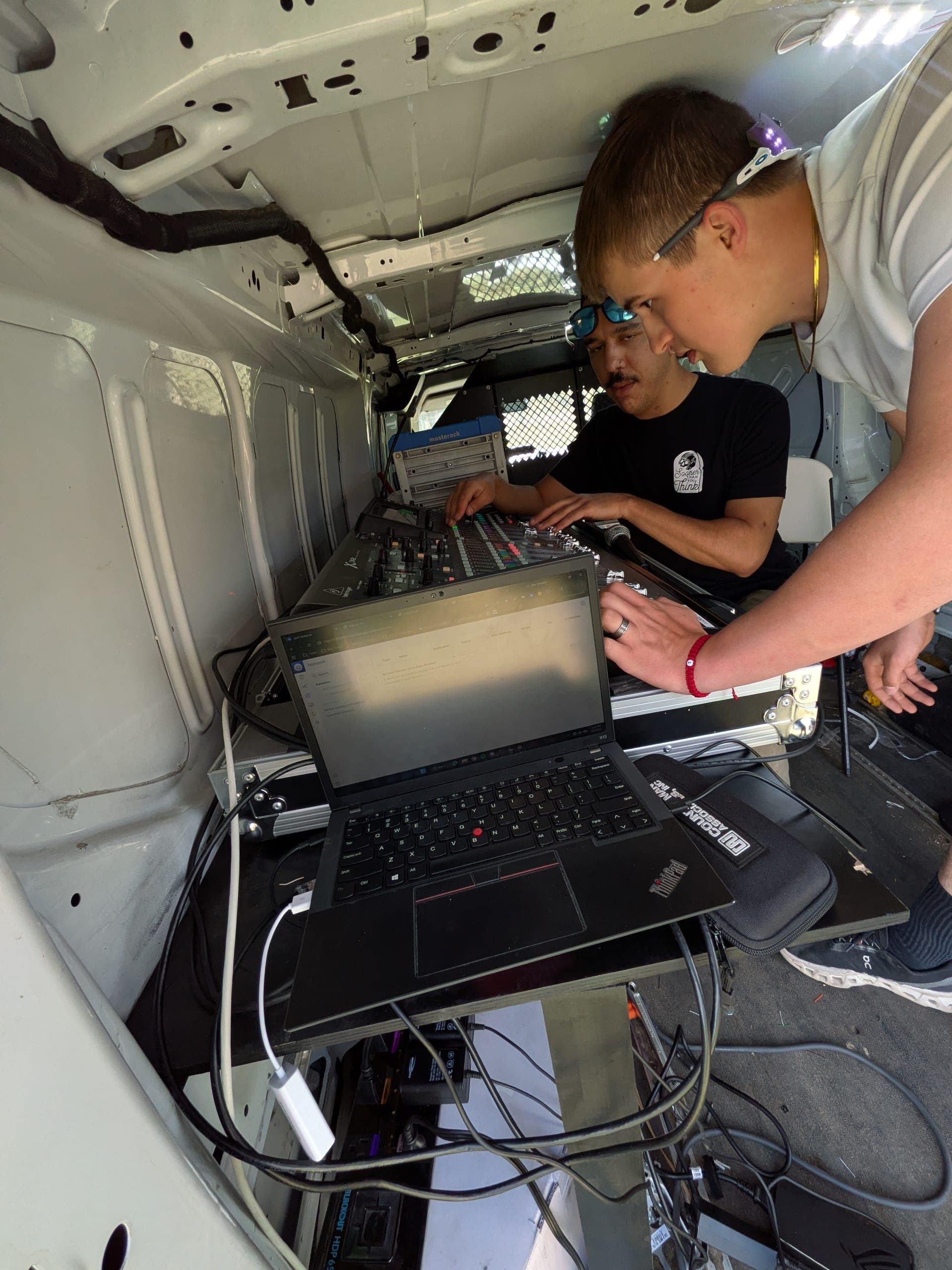 Two Brink crew members working on an X32 mixing console and a laptop inside the van
